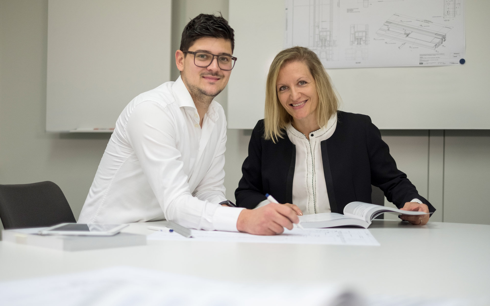 Zwei Personen arbeiten gemeinsam an technischen Zeichnungen im Büro