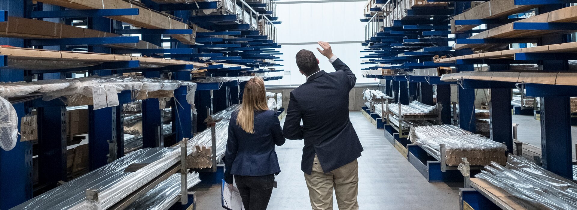 Lagerhalle mit Metallprofilen und Personen bei der Bestandsaufnahme