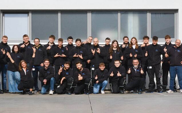 Gruppenfoto eines Teams vor einem Gebäude mit Daumen-hoch-Gesten