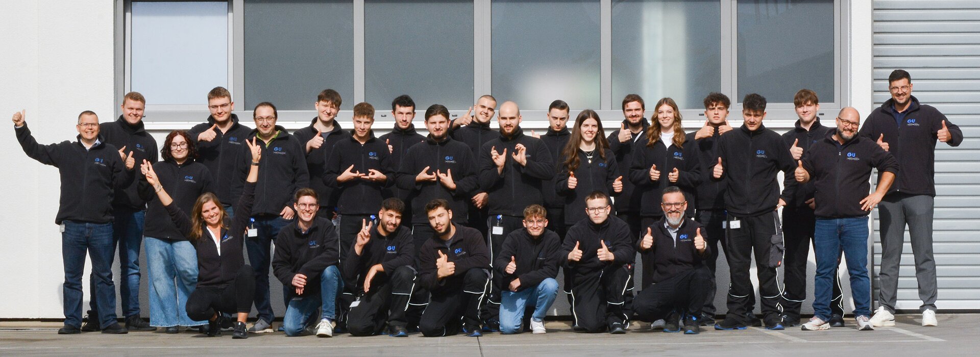 Gruppenfoto eines Teams vor einem Gebäude mit Daumen-hoch-Gesten