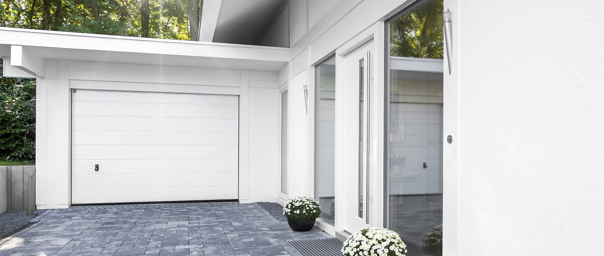 Modernes Einfamilienhaus mit weißer Garage mit gepflasterter Auffahrt und Hauseingang mit Glastür