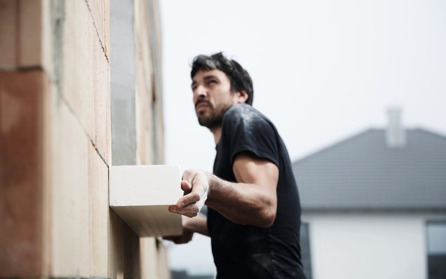 Bauarbeiter montiert GU-Vorbauzarge an eine Hauswand beim Rohbau